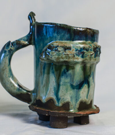 Green medieval ceramic tankard with a textured band, curved handle and small dark clay feet