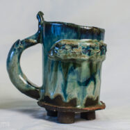 Green medieval ceramic tankard with a textured band, curved handle and small dark clay feet