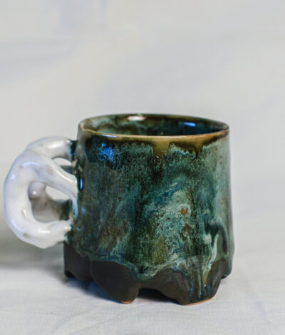 Sculptural green ceramic mug with a white loop handle, handmade from dark stoneware