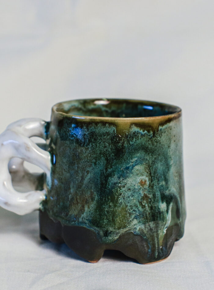 Sculptural green ceramic mug with a white loop handle, handmade from dark stoneware