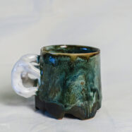 Sculptural green ceramic mug with a white loop handle, handmade from dark stoneware